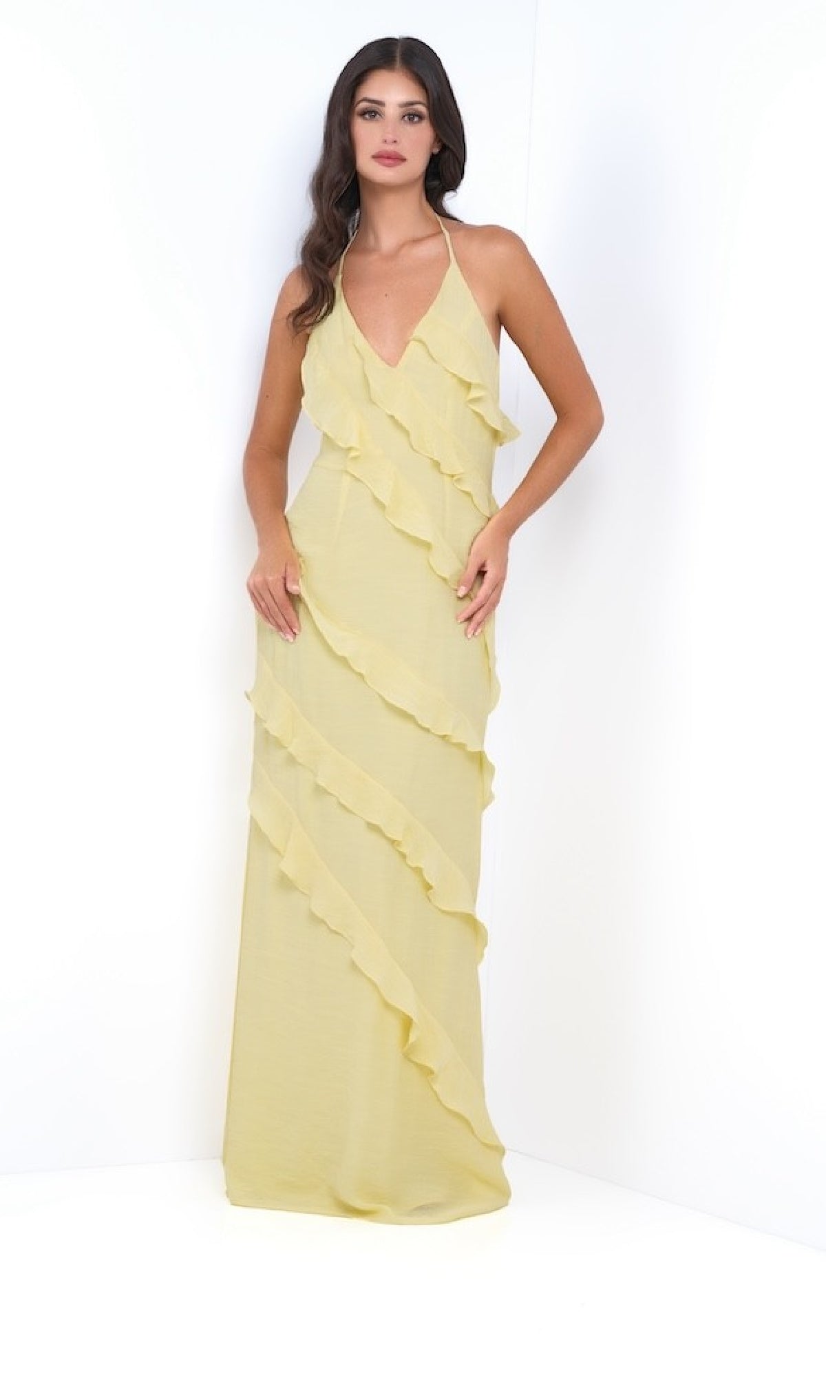 A woman stands against a white background wearing the Remi by Velvi, a V-Neck Halter Ruffled Long Prom Dress in light yellow with diagonal layers.